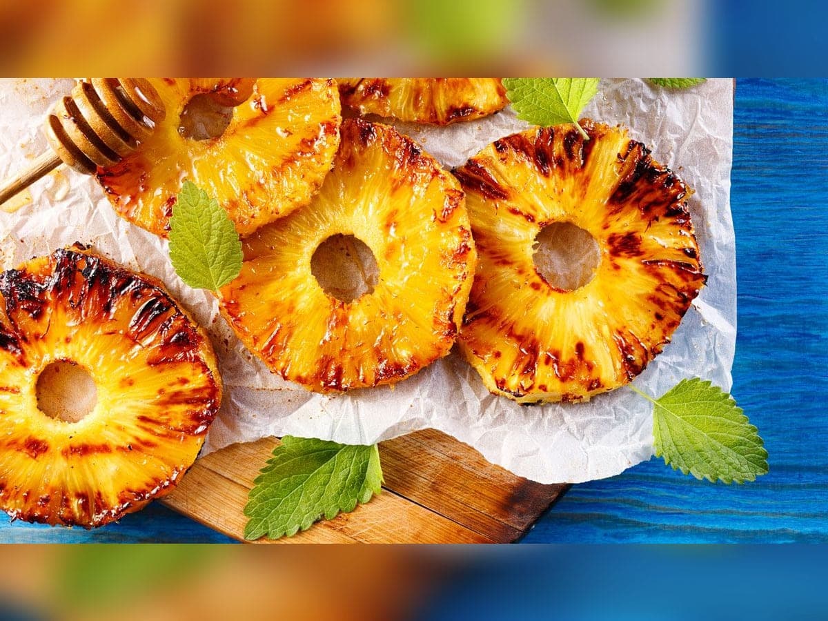 Rodajas de piña a la parrilla caramelizadas con azúcar morena y canela sobre papel para hornear