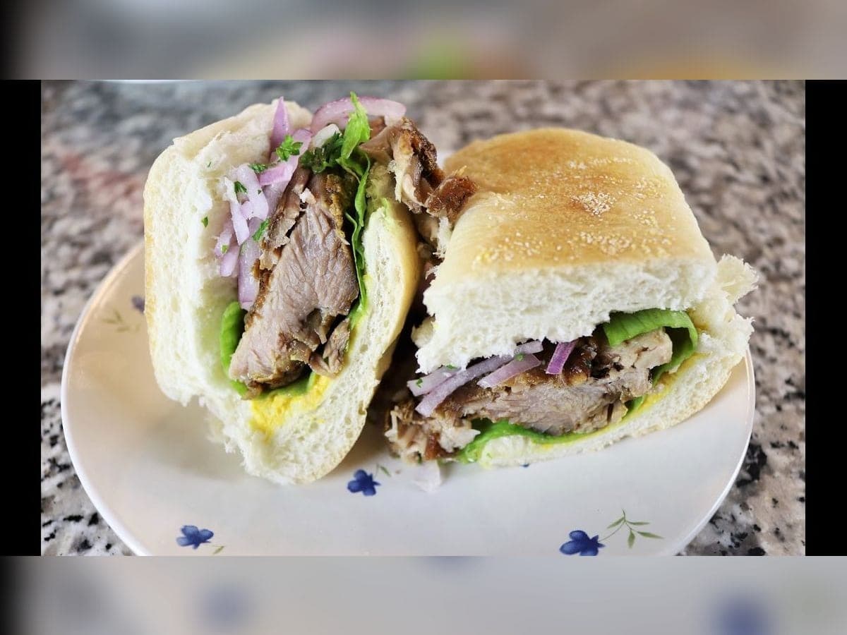Sándwich de pan canilla relleno de pernil horneado, tomate, queso y lechuga