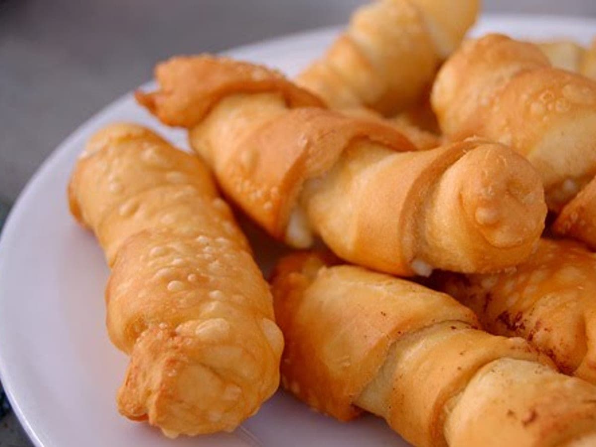 Tequeños fritos y dorados, apilados en un plato, con el queso asomando