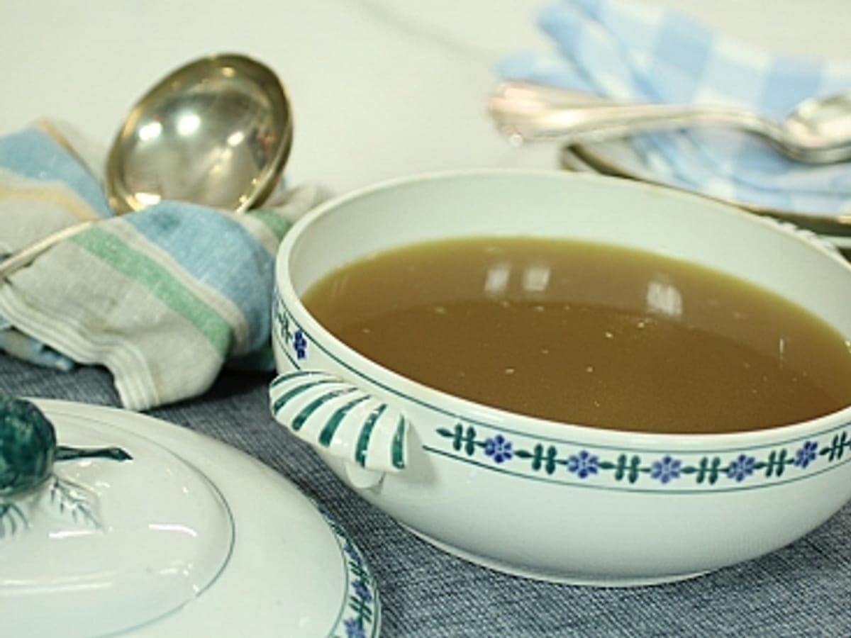 Taza de consomé de sardinas claro, servido con un gajo de limón