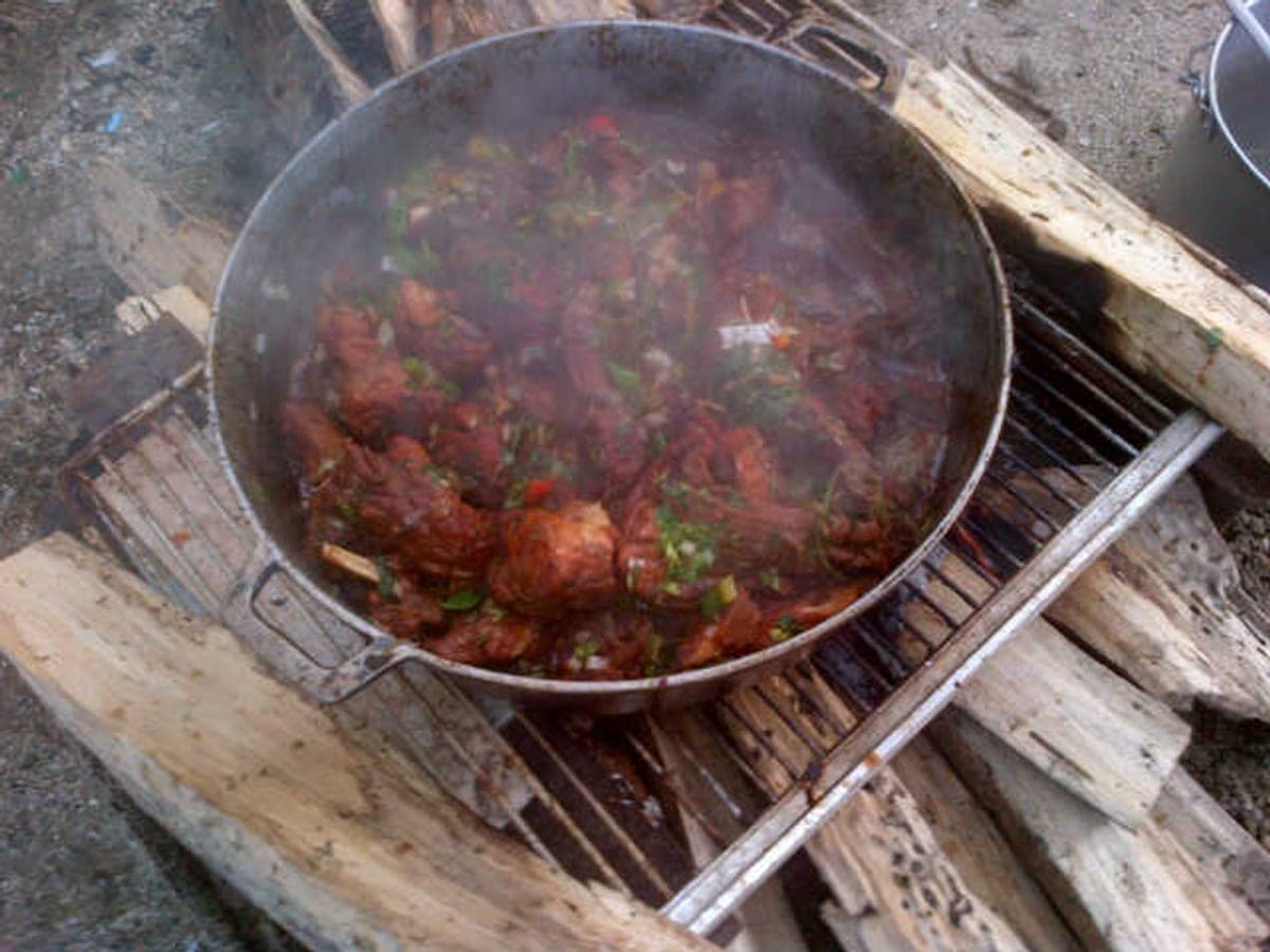 Guiso de lapa cocinándose en un caldero de hierro sobre leña, con su salsa espesa y humeante
