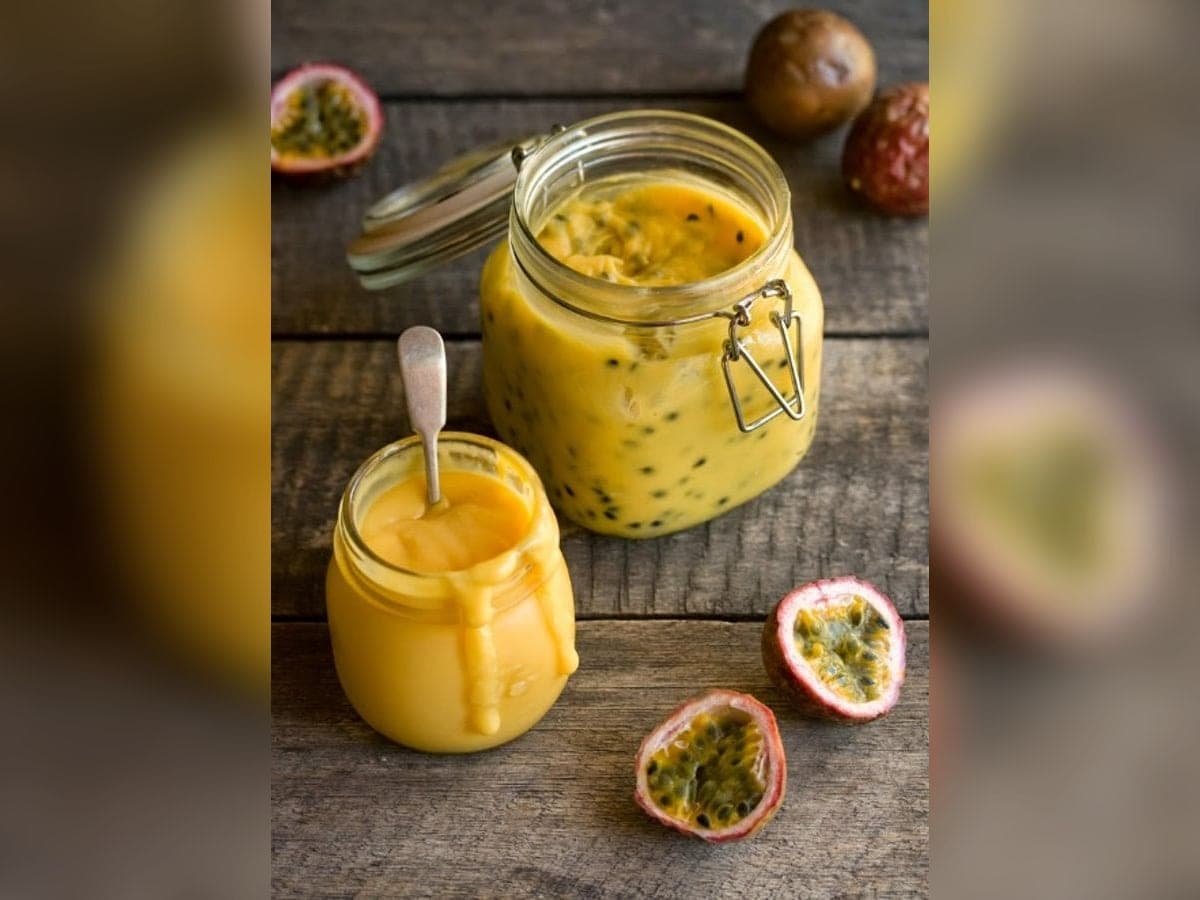 Frasco de vidrio con mermelada de parchita anaranjada y una cuchara al lado