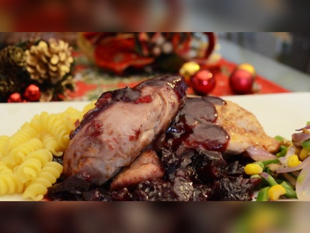 Presas de pavo bañadas en salsa oscura de papelón y ciruelas pasas, servidas con puré de papas y ensalada en una mesa navideña
