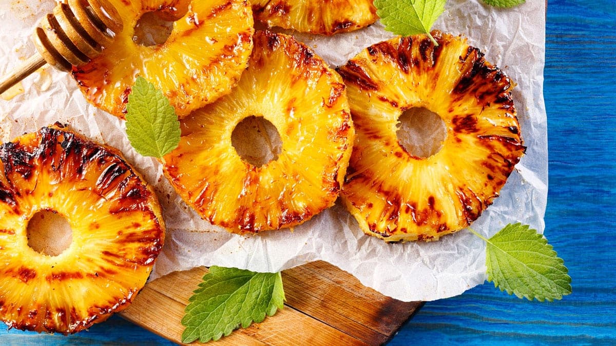 Rodajas de piña a la parrilla caramelizadas con azúcar morena y canela sobre papel para hornear