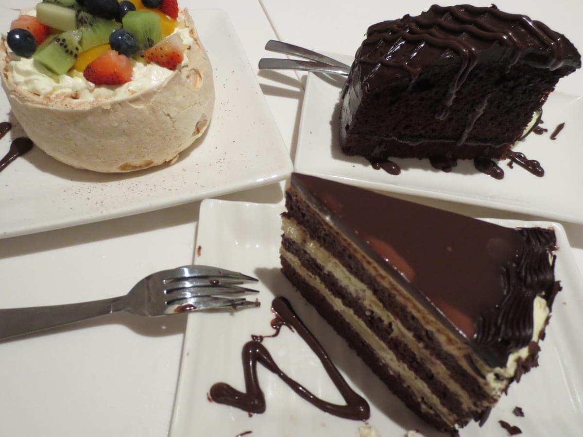 Porción de torta de chocolate de tres capas con relleno claro de queso y cubierta espejo